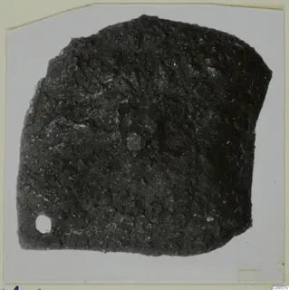 Corroded bronze mounting fragment with a small hole near the lower left corner