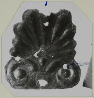 Bronze mounting fragment from Vouni with a fan-shaped top of radiating ridges and two round scrolls at the base.