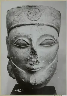 Limestone head sculpture with a tall cylindrical headdress decorated with a rosette, nose broken