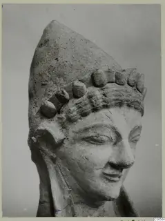 Terracotta head of a figure with a tall pointed headdress studded with knobs, from Mersinaki