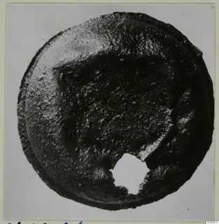 Round corroded bronze fragment with a broken hole at the lower edge, photographed from above on a mount.