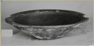 Pottery coarse ware bowl with two small horizontal handles and a dark interior, photographed as a find