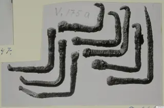 Several corroded bent metal rods with knobbed ends, arranged on a grey card mount