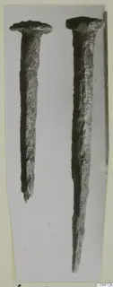 Two corroded metal nails with flat heads, shown upright side by side against a grey background, from Vouni T. 1-16