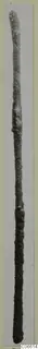 Long, thin, corroded metal rod photographed upright against a pale background