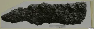 Corroded iron tool fragment from Vouni, long and tapering to a point at the left