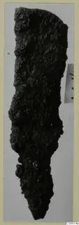 Corroded iron tool fragment from Vouni, long and narrow, tapering to a point at the bottom