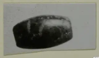 Dark barrel-shaped bead from Vouni, the Korakas tombs, shown close up