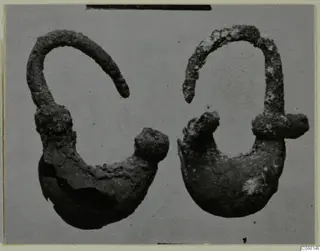 Two corroded metal ornaments, each with a curved wire loop and a rounded lower part with a knob