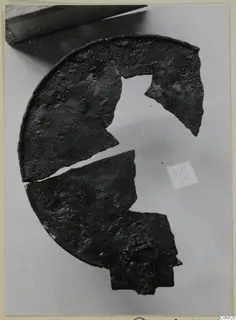 Broken fragments of a round bronze disc with a raised rim, on a pale background