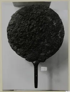 Bronze mirror with a long handle, its disc surface heavily corroded and pitted.