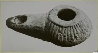 Terracotta oil lamp with a long spout and a round filling hole, its shoulder decorated with radiating grooves.