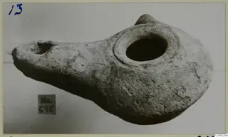 Terracotta oil lamp with a large central filling hole and a nozzle at the left end.