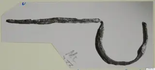 Fibula fragment of bronze from Mersinaki: a long thin pin bent into a curved loop at one end.