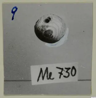 Round bead with a hole near the top, from Mersinaki, photographed on grey card.