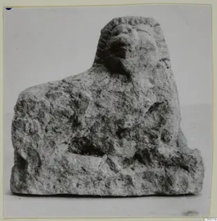 Small limestone figure of a crouching animal with a mane-like head, shown against a plain background.