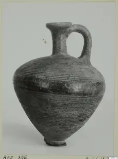 Black Lustrous Ware juglet with a single loop handle and horizontally ribbed body, shown against a grey backdrop