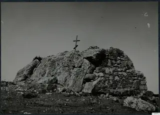 Built tomb of dressed stone with a wooden cross standing on top of a rocky mound