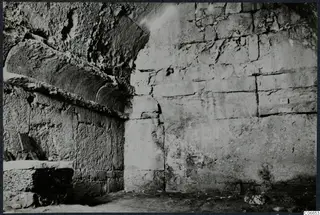 Interior of a built tomb chamber with large stone walls, a squared stone block and a small object at left