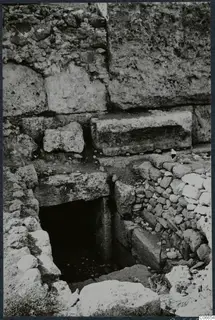 Built tomb with a dark doorway at the foot of stone steps, set among large masonry blocks and rubble walls