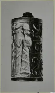 Cylindrical seal carved in relief with a standing figure in a long robe and spiral motifs, photographed on a grey card.