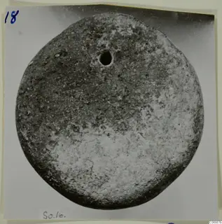 Round disc-shaped find with a small hole near its upper centre, photographed on a mounted card, from Soli