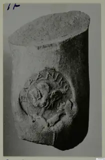 Cylindrical object with a raised circular medallion showing a head in profile and partly legible letters around its rim