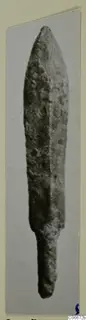 Bronze dagger blade with a pointed tip and short tang, photographed against a grey background.