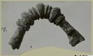 Corroded bronze arch-shaped adornment with knobbed and ribbed segments, shown on a mounted print from Soli