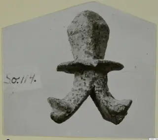Corroded metal object with a rounded upper part, a flat flange across the middle and two splayed prongs below