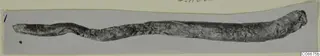 Long, corroded lead object lying horizontally, with a slight bend and a knobbed right end