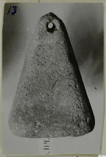 Triangular object with a round perforation near its narrow end, photographed against a dark grey backdrop