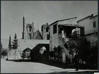Church ruin with a tall pointed tower behind an arched stone wall at Famagusta, with a man standing in the street