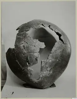 Broken pottery jug from Lapithos, partly reassembled from fragments, standing on a small wooden stand.