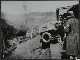 Car tilted on a dirt track at Kythrea, its rear wheel up on a stone bank, with a man leaning into it