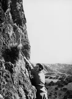 Joan du Plat Taylor climbing a rock face at Fylleri, reaching up toward the cave