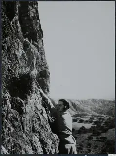 Joan du Plat Taylor climbing a rock face at Fylleri, with a valley and hills stretching behind her.