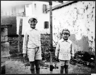 Martin and Stefan Gjerstad standing in a yard in Nicosia beside a metal pipe with a tap, in front of a white wall.