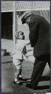 A man in a flat cap and dark coat bends down to play with a small child in a courtyard in Nicosia