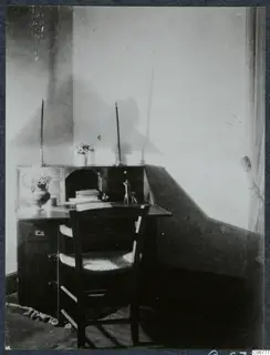 Living room corner with a wooden desk, a chair with a woven seat, and a vase of flowers on the desk.