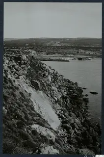 Rocky coastline with a steep cliff falling to the sea, with low hills behind