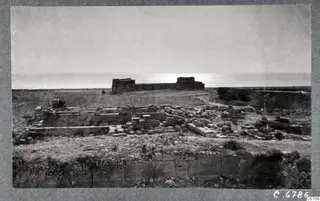 Ruins of the Temple of Aphrodite at Kouklia: low stone walls and scattered blocks, with a ruined building and the sea beyond