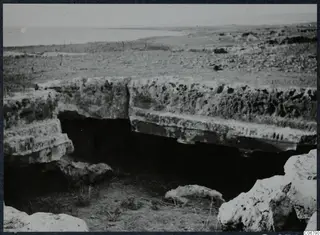 Pale weathered stone slabs over a dark recess, with flat land and sea behind