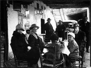 Lunch break at a table on a covered terrace in Skarinou, with adults and two boys seated and men standing nearby
