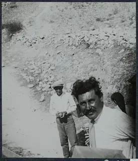 Two men on a stony slope at Mersinaki, the nearer one in the foreground looking at the camera, the other in a flat cap behind him.