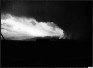 Storm clouds lit against a dark sky above low, dark mountains in a wide landscape
