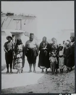 The priest and his family standing in a village street at Mandres, in front of a whitewashed building with a wooden door