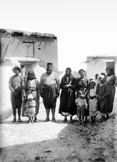 The priest and his family standing in a dirt street at Mandres, in front of plastered mud-brick houses