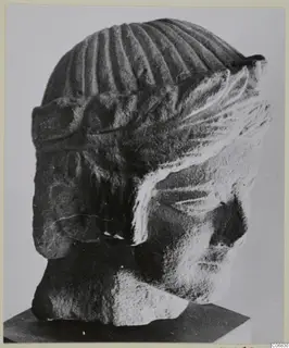 Limestone sculpture head from Mersinaki, shown in side view on a dark stand.