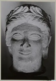 Limestone head of a figure with carved wavy hair and a slight smile, seen from the front